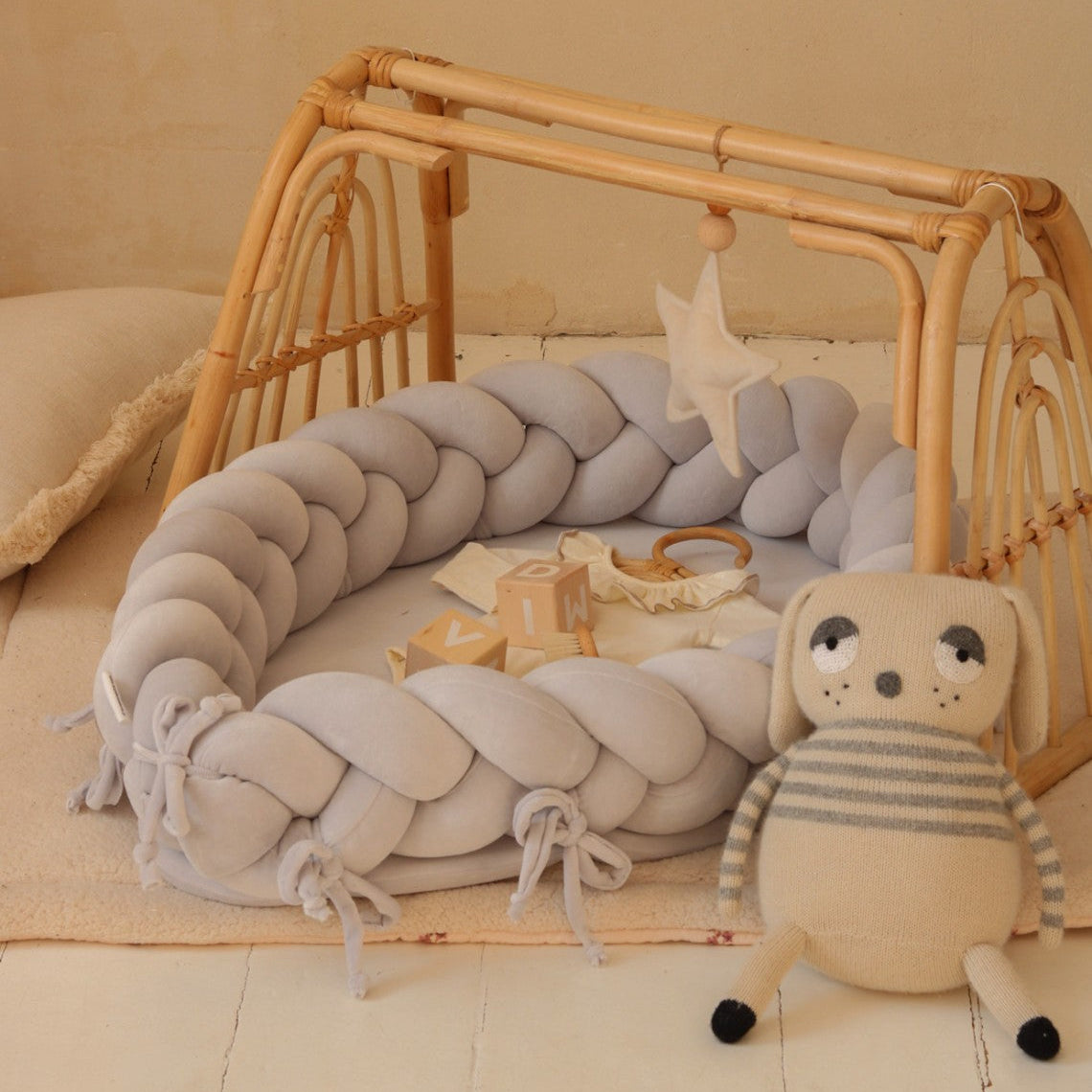 Baby crib with braided gray bumper, plush toy, and baby items on a beige background