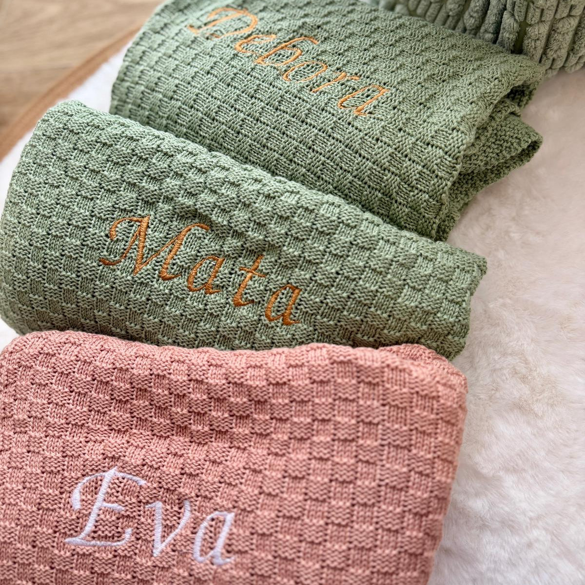 Three folded towels in green and pink with embroidered names on a light background