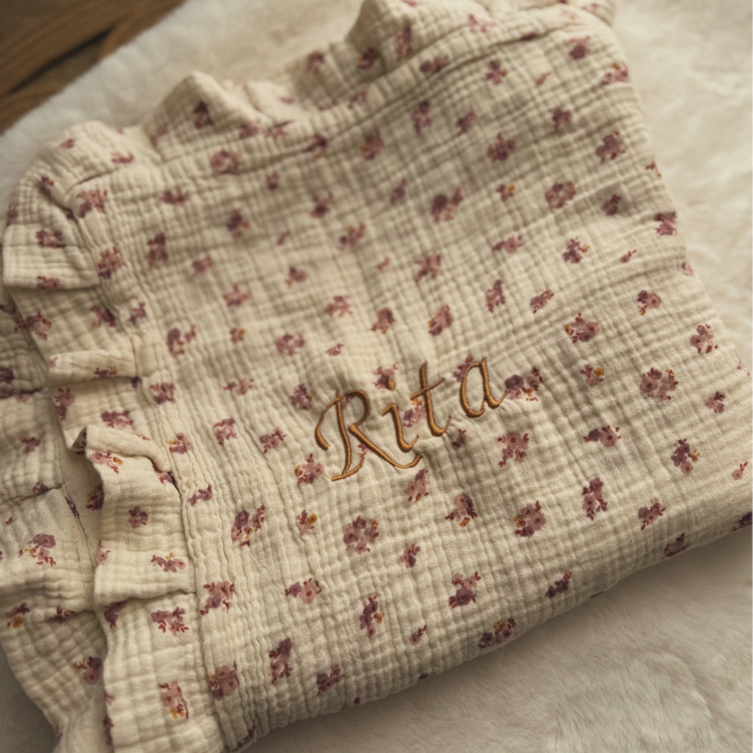 Floral-patterned fabric with 'Rita' embroidered on it, lying on a textured surface.