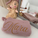 Pink plush toy with 'Mara' embroidered on it, next to a mirror.