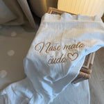 White baby outfit with embroidered text on a polka dot surface
