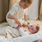 Baby Natur white sleeveless sleeping bag with yellow lemon print, worn by a boy interacting with a baby.