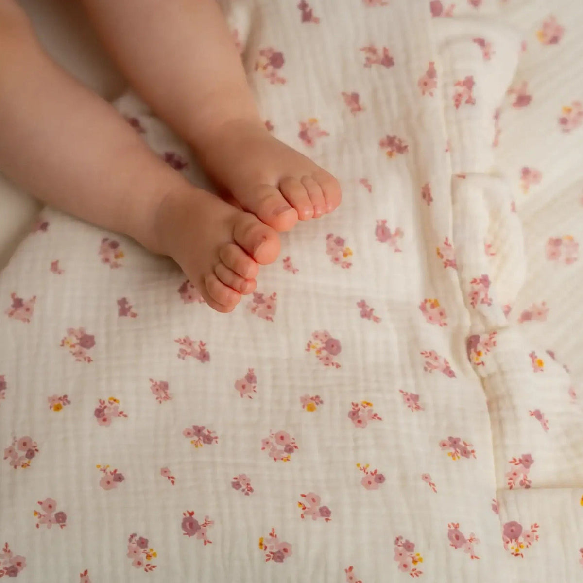 Baby Natur Tetra muslin bedding with a delicate floral print in pink and yellow on a cream background. Features ruffled edges and is made from 100% organic cotton.
