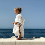 Baby Natur white muslin poncho with cherry print, featuring side ties and a hood. Perfect for beach or pool.