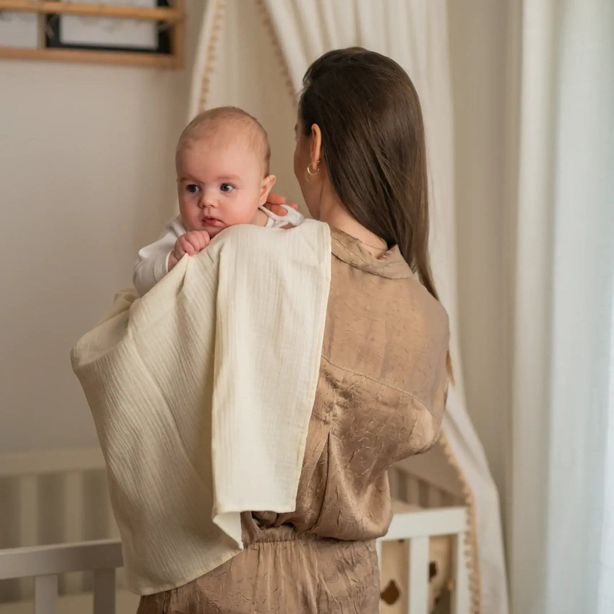 Baby NaturA cream 100% cotton muslin tetra diaper draped over a woman's shoulder holding a baby.