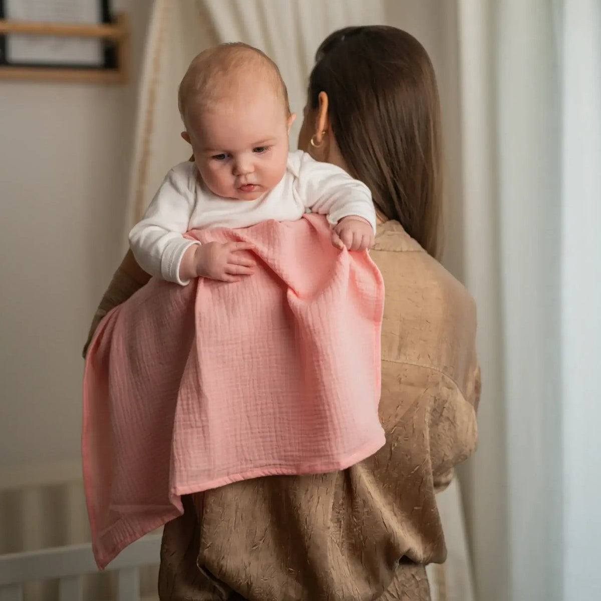 Baby Natur pink 100% cotton muslin swaddle blanket draped over a baby held by a woman.